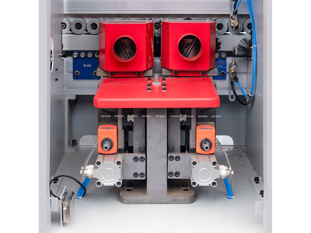 Gluing station inside an edge banding machine, showing the glue pots, pressure rollers and pneumatic cylinders